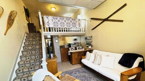 A cozy living room with a white sofa, wooden coffee table, and a patterned rug. A staircase leads to an upper level with a balcony. - Cozy Alpine Retreat in Historic Downtown (McGregor)