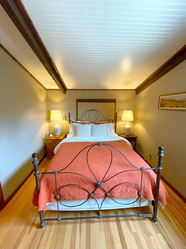 Un lit bien fait, avec un cadre en métal, deux tables de chevet avec des lampes et un plancher en bois.