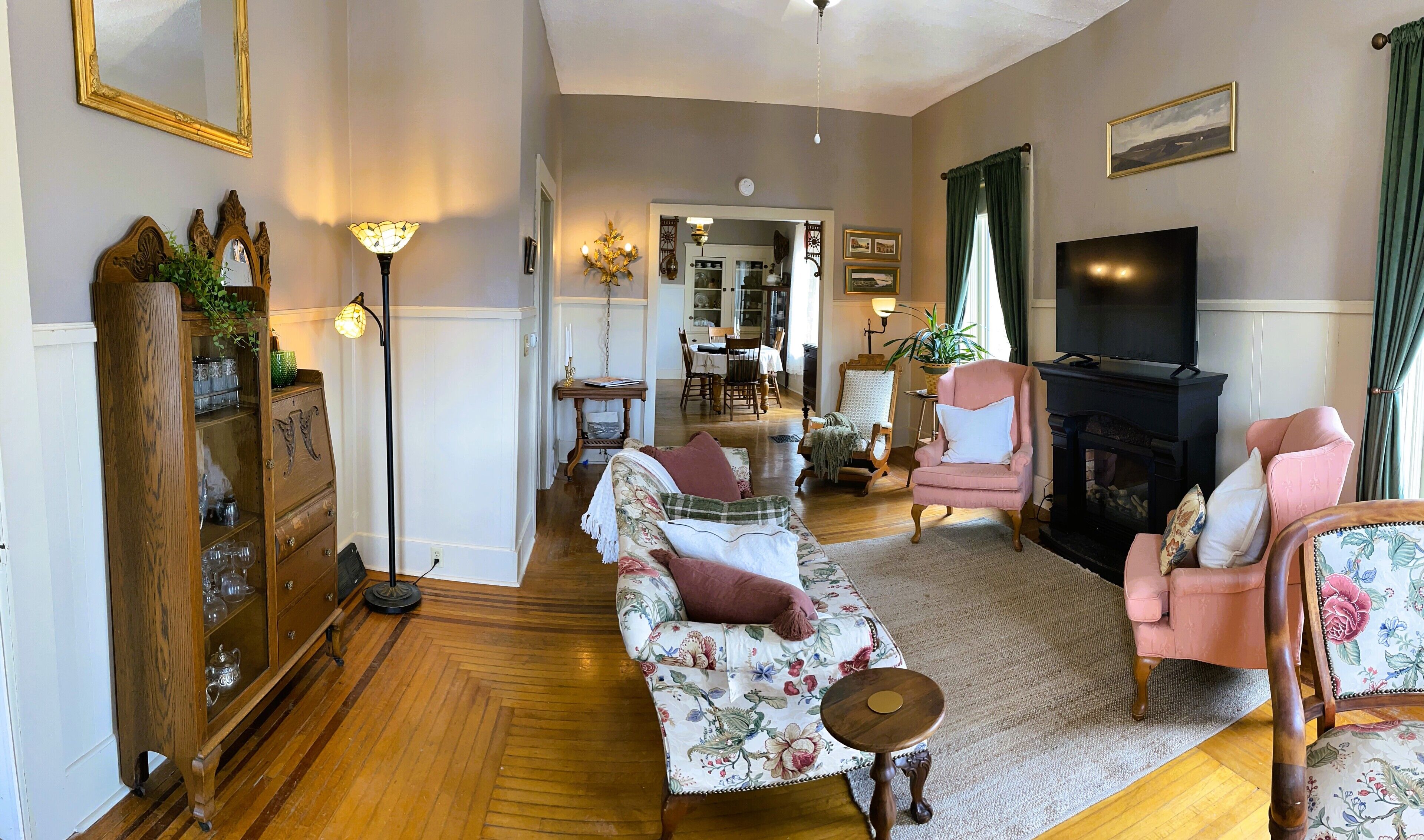 Een woonkamer met een bank, fauteuils, een houten kast, een televisie en een open haard.