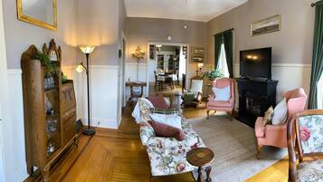 Een woonkamer met een bank, fauteuils, een houten kast, een televisie en een open haard.