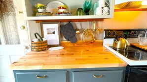 A kitchen with a wooden countertop, a stove, and a cabinet with dishes and utensils.