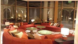 Een hal met een rode zithoek, meerdere ronde tafels en grote ramen met uitzicht op het interieur.