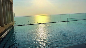 Een zwembad met een glazen barrière en uitzicht op de ondergaande zon over het water.