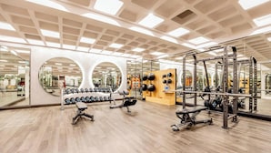 Een moderne sportschool met spiegelwanden, diverse gewichthefapparaten en een houten vloer.