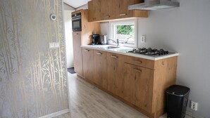 A compact kitchen with wooden cabinets, a gas stove, and a window providing natural light. - Heivlinder Comfort 4p (Ermelo)