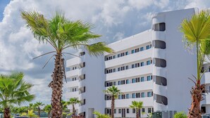 Un edificio moderno a più piani con balconi, circondato da palme e un cielo sereno.