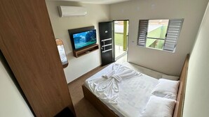 A bedroom with a bed, a TV mounted on the wall, and a sliding door leading to a balcony. - Pousada Capiau  (Bonito)
