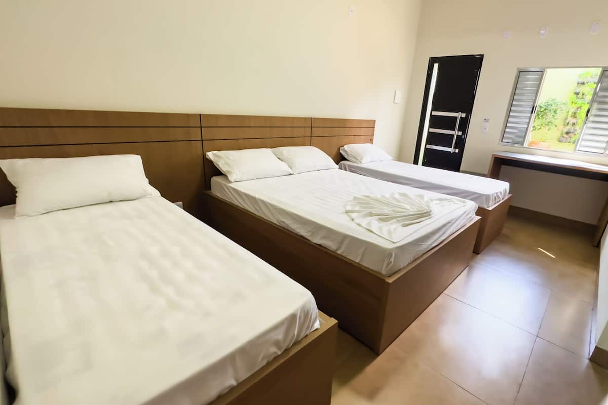 A hotel room with two beds, a wooden headboard, a desk, and a window with blinds.