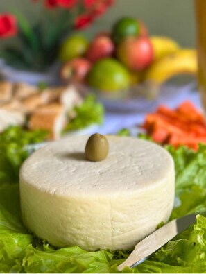 A round cheese wheel on a bed of lettuce with a knife beside it. - Pousada Capiau  (Bonito)