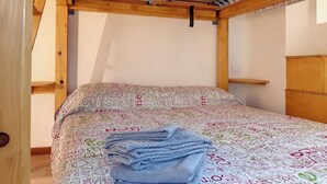 Ein Einzelbett mit gemustertem Bettbezug, einem Holzkopfteil sowie einer Decke mit freiliegenden Balken und Haken.