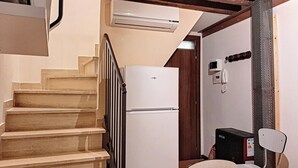 Eine kleine Küche mit einem weißen Kühlschrank, einem Tisch mit Stühlen und einer Treppe, die zu einer oberen Ebene führt.