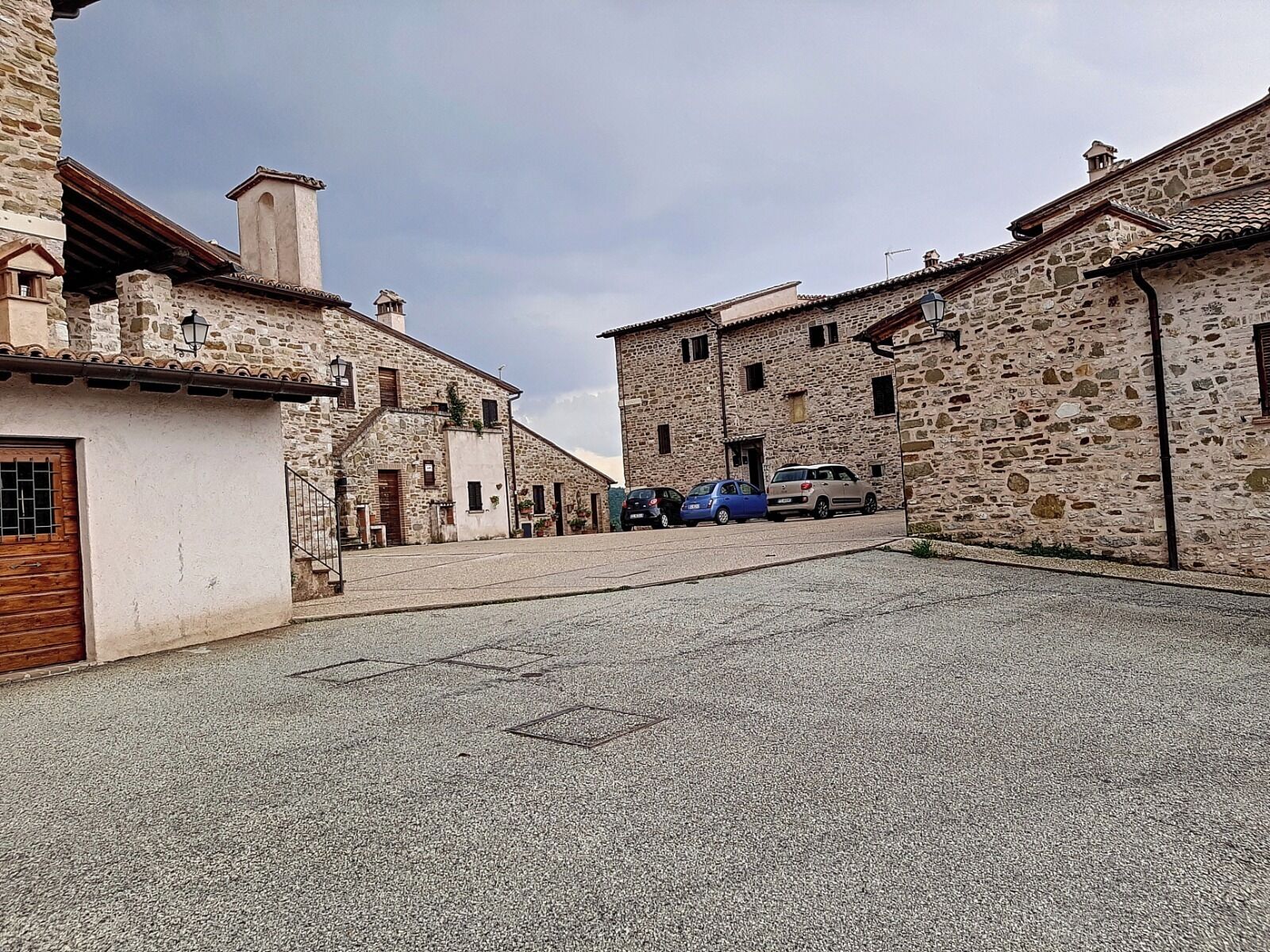 Une rue étroite bordée d’immeubles en pierre, quelques voitures garées et un ciel dégagé.