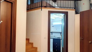 A hallway leading to a bathroom with a tiled floor, a wooden staircase, and a metal railing on the upper level. - Appartamenti Giove - Trilocale by Ospitaci (Giove)