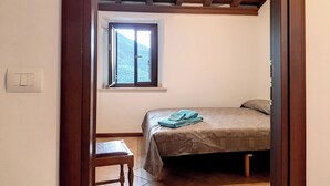A bedroom with a single bed, a window, a small table, and a wooden ceiling. - Appartamenti Giove - Trilocale by Ospitaci (Giove)