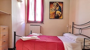 A bedroom with a bed, a radiator, a window with curtains, a dresser, and a painting on the wall.