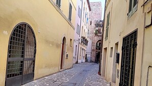 A narrow cobblestone street flanked by buildings with arched doorways and barred windows.