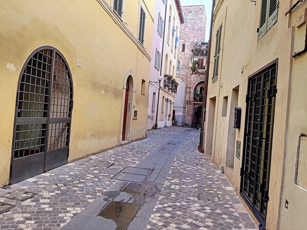 A narrow cobblestone street flanked by buildings with arched doorways and barred windows.