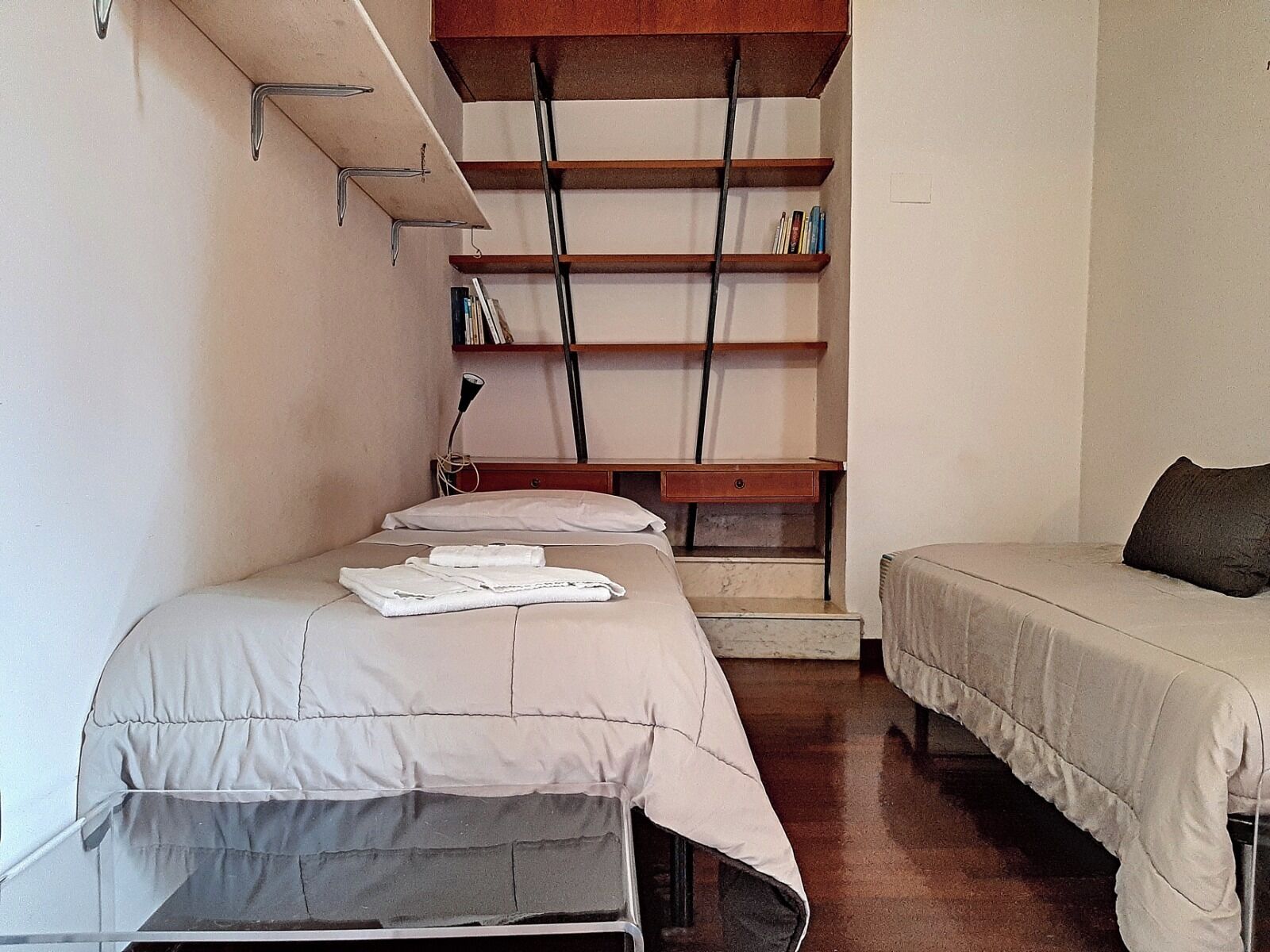 Une petite chambre avec deux lits, un bureau et une étagère remplie de livres.