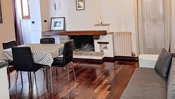 Een woonkamer met een open haard, houten balken, een eethoek met stoelen, een bank en een raam met gordijnen.