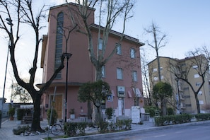Un immeuble à plusieurs étages, doté d’une façade rose, d’une entrée bien visible et d’une enseigne indiquant qu’il s’agit d’un établissement commercial.