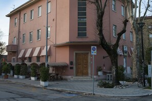 A pink building with a central entrance, outdoor seating, and a no parking sign.