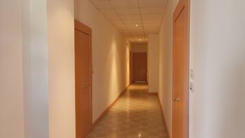 A long, narrow hallway with wooden doors on both sides and a checkered floor.