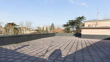 A rooftop terrace with a tiled floor, surrounded by buildings and trees.