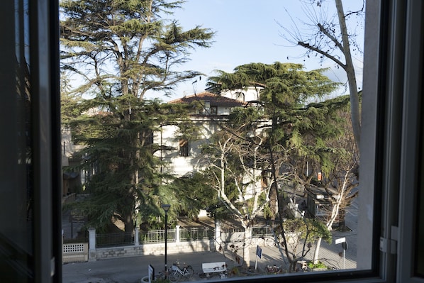 A view of a building with a tiled roof, surrounded by trees and a street with bicycles and a bench.