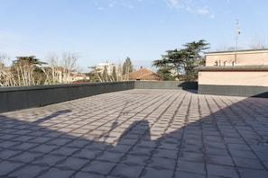 Una terrazza sul tetto con pavimento piastrellato, circondata da edifici e alberi.