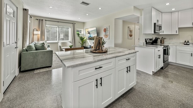 A modern kitchen with white cabinetry, a marble countertop, and a dining area with a sofa and table. - Family-Friendly 3BR | Downtown & Lake Hollingsworth (Lakeland)