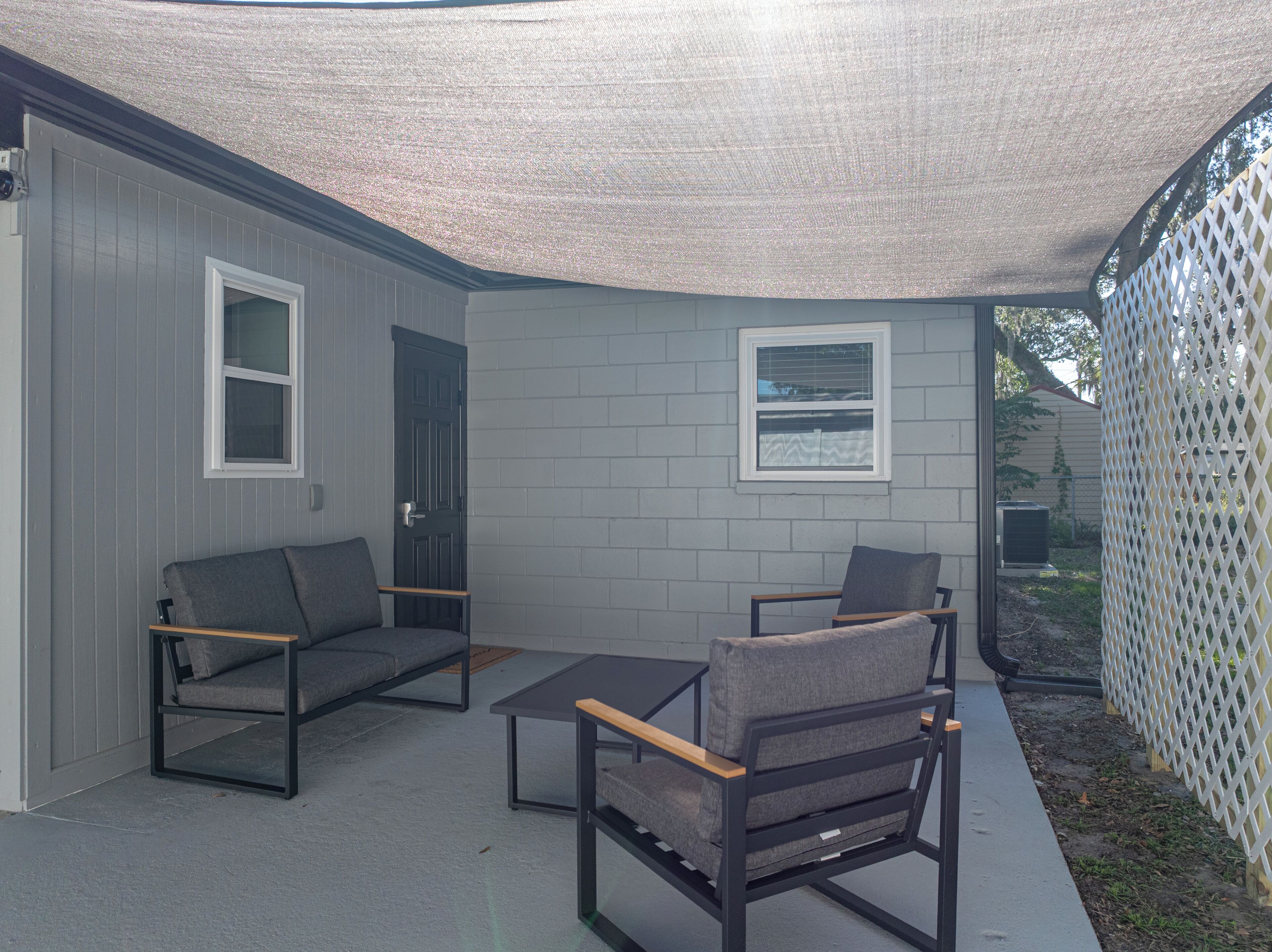 A covered patio area with a gray sofa, a wooden coffee table, and two chairs.