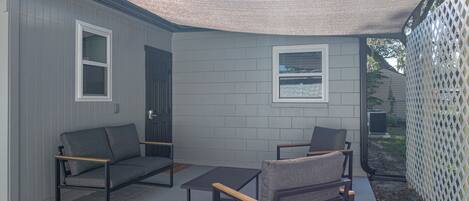 A covered patio area with a gray sofa, a wooden coffee table, and two chairs.
