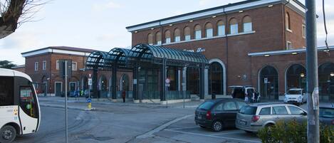 A building with a glass entrance canopy, a brick facade, and a parking area with cars.
