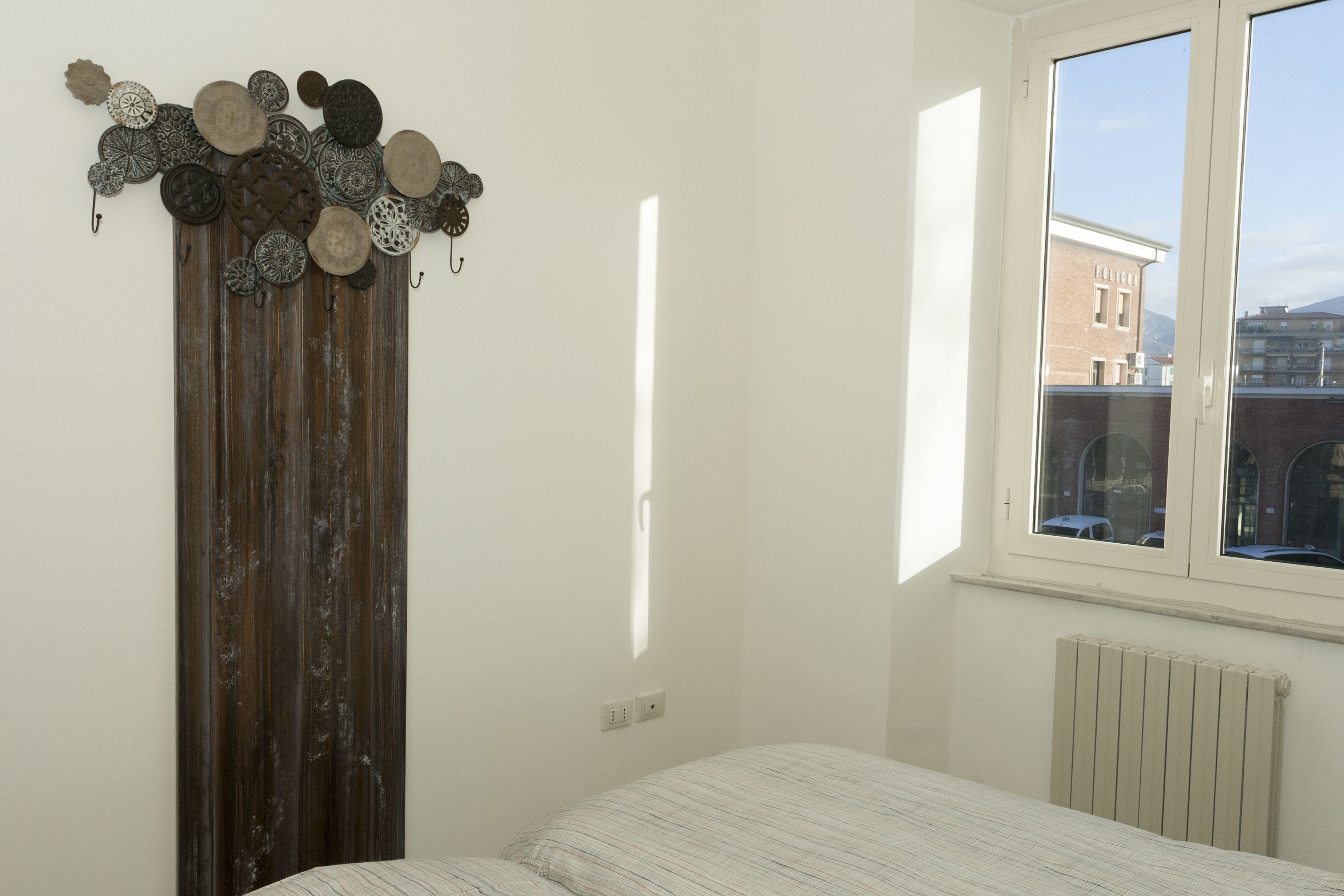 Ein Schlafzimmer mit einem Bett, einem Holzschrank und einem Fenster mit Blick auf Gebäude.