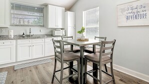 Een moderne keuken met witte kastjes, een magnetron en een eethoek met een tafel en stoelen.