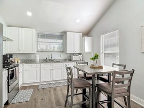 Una cocina moderna con armarios blancos, una mesa de comedor con sillas y una planta en maceta sobre la mesa.