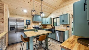 A modern kitchen with wooden ceiling, stainless steel appliances, and a central island with bar stools. - Greenhouse Cabin • Forest Views & Serenity (Cosby)