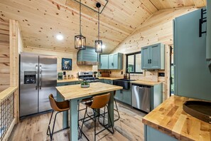A modern kitchen with wooden ceiling, stainless steel appliances, and a central island with bar stools. - Greenhouse Cabin • Forest Views & Serenity (Cosby)
