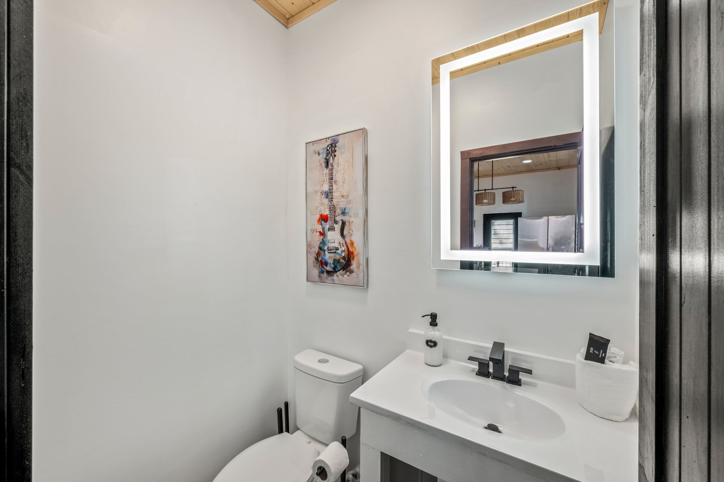 A modern bathroom with a white sink, a mirror with a light, and a toilet.