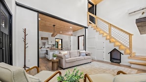 Amplia sala de estar con sofá, sillas, una planta en maceta y una escalera con barandillas de madera.