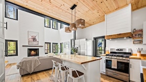 Una cocina moderna con una isla central, taburetes de bar, una chimenea y un amplio ventanal con vistas al exterior.