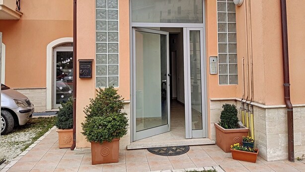 Entrada d'un edifici amb una porta de vidre, plantes en testos i un cotxe aparcat.