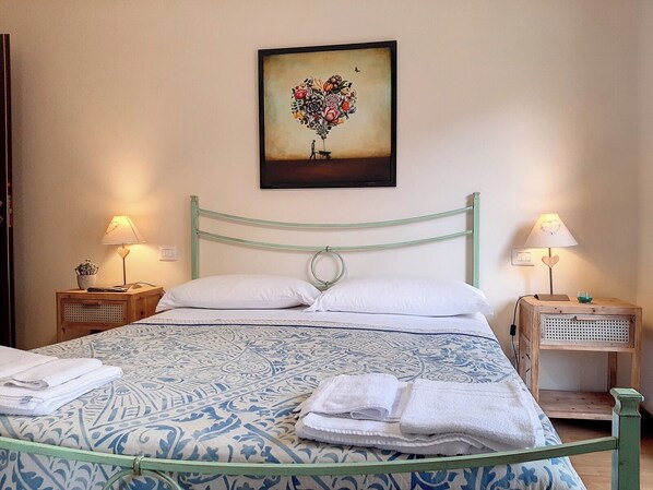 Un lit bien fait, recouvert d’une couvre-lit à motifs, deux tables de chevet avec des lampes et un tableau de fleurs accroché au mur.