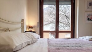 Un dormitorio con cama, una mesita de noche con lámpara, una ventana con vistas a árboles y una pared decorada con cuadros.