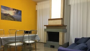 A dining area with a table and chairs, a fireplace, a sofa, and a painting on the wall. - Via Oberdan 113 by Ospitaci (Foligno)