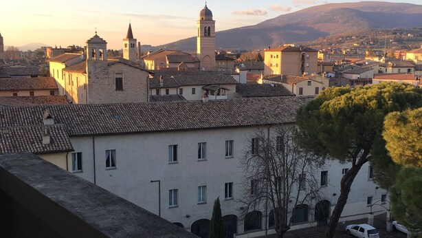 A view of a town with historic buildings, a prominent tower, and a mountain in the background. - Via Oberdan 113 by Ospitaci (Foligno)
