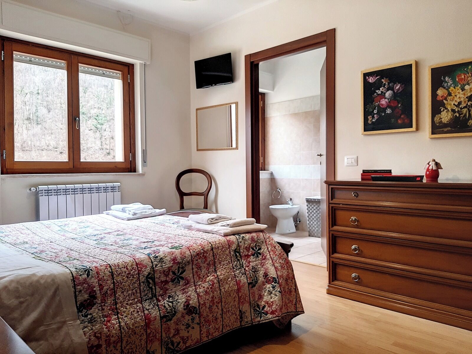 Un dormitorio con cama, cómoda de madera y baño a la vista a través de una puerta abierta.