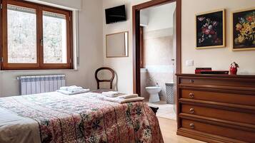 Un dormitorio con cama, cómoda de madera y baño a la vista a través de una puerta abierta.