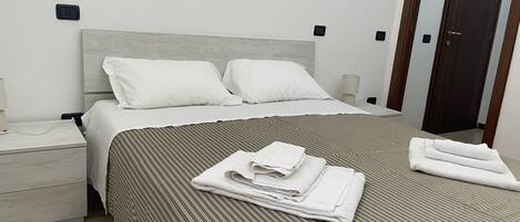 A neatly made bed with white linens and striped bedding, a bedside table with a lamp, and a door in the background.