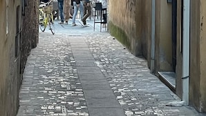 A narrow alleyway with cobblestone pavement, a blue directional sign, and a group of people gathered around a table.